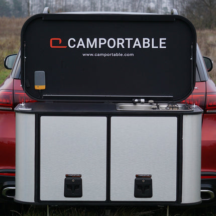 Camportable camping kitchen hitch mounted on a red car in an outdoor setting